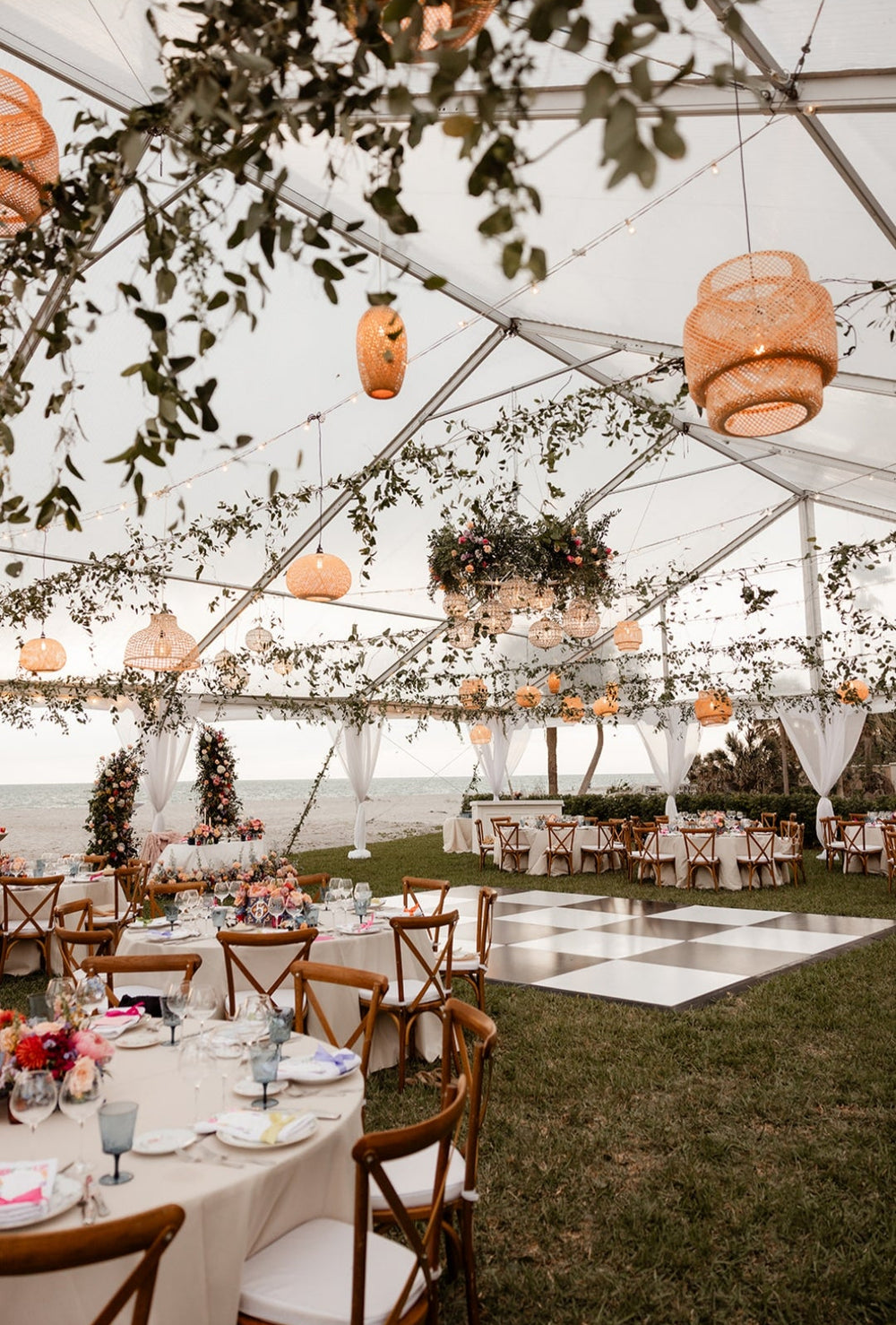 Outdoor wedding reception with hanging greenery, lush centerpieces, and a chandelier made of flowers.
