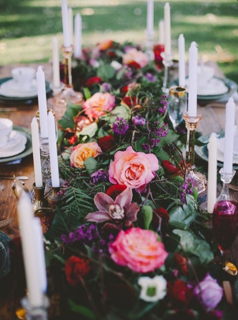 Table setting with taper candles and colorful garland. Loscious greenery, sunset free spirit garden roses, cymbidium orchids and other jewel toned flowers..