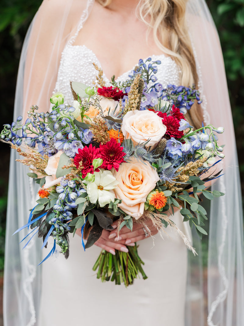 Bride holding a colorful bouquet of flowers with a veil and greenery in the background
