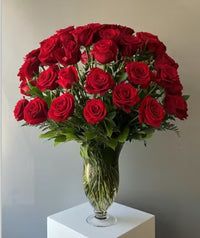 A Stunning display of 48 long stem roses with lush greenery arranged in a clear glass vase.